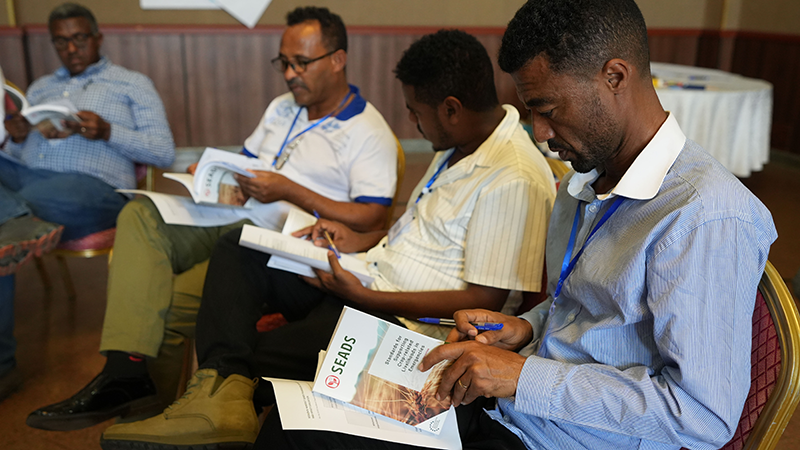 Four men seated reading SEADS handbook