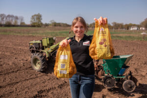 Smiling person stands in field holding two bags of seeds