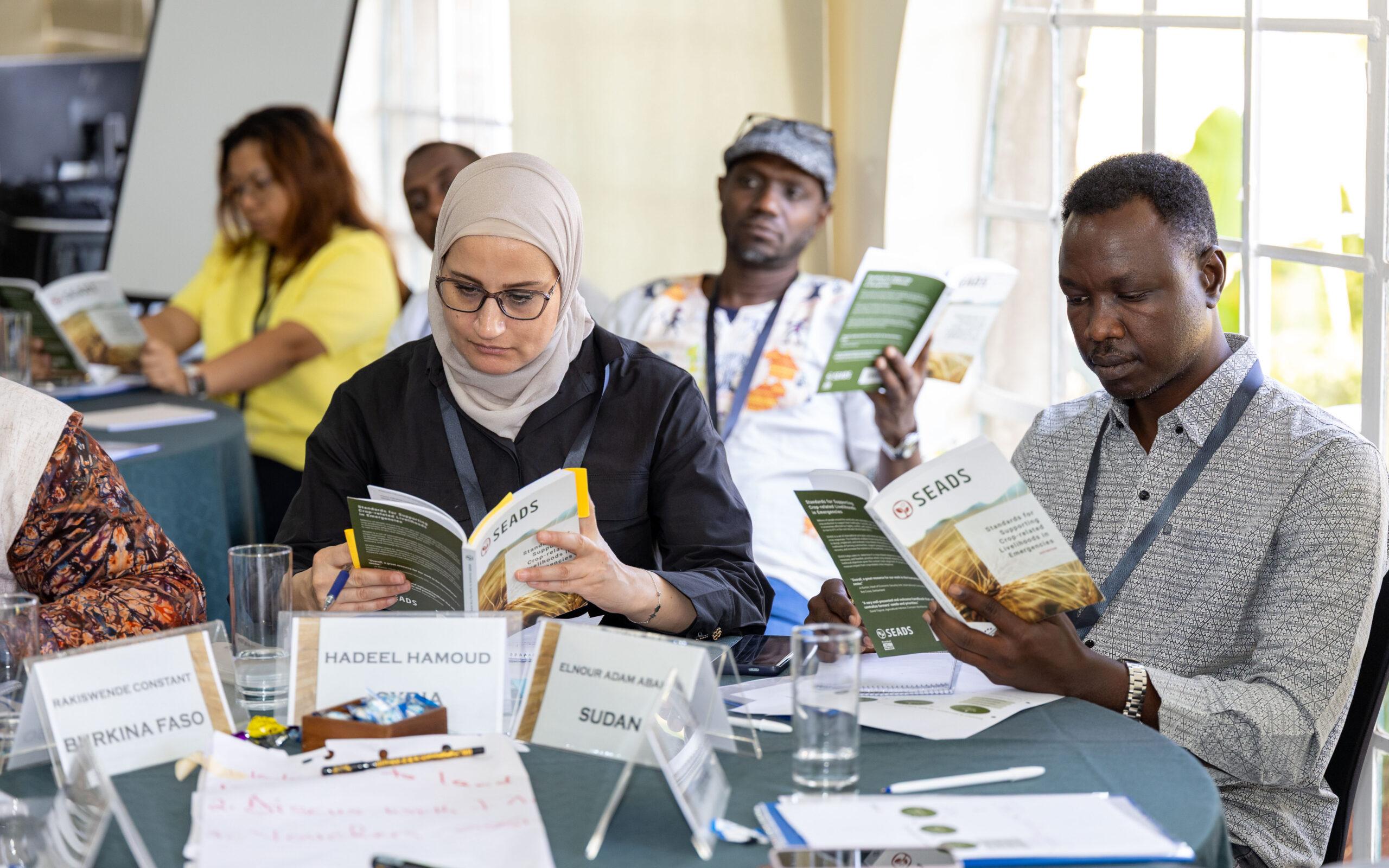 A group of people sitting around tables, all reading their SEADS Handbooks
